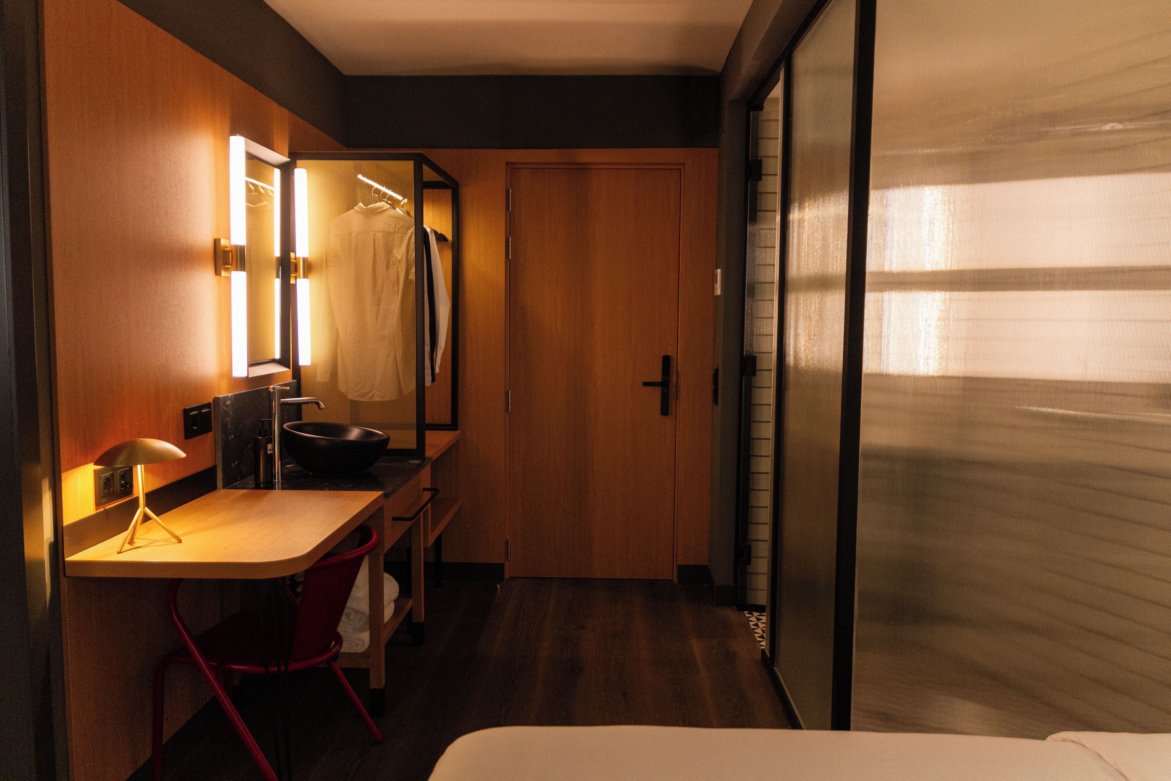 Een hotelkamer met een houten bureau, een stoel, een spiegel en een bed.