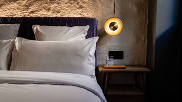 A bedroom with a bed, pillows, a bedside table with a glass of water, and a wall-mounted light fixture.