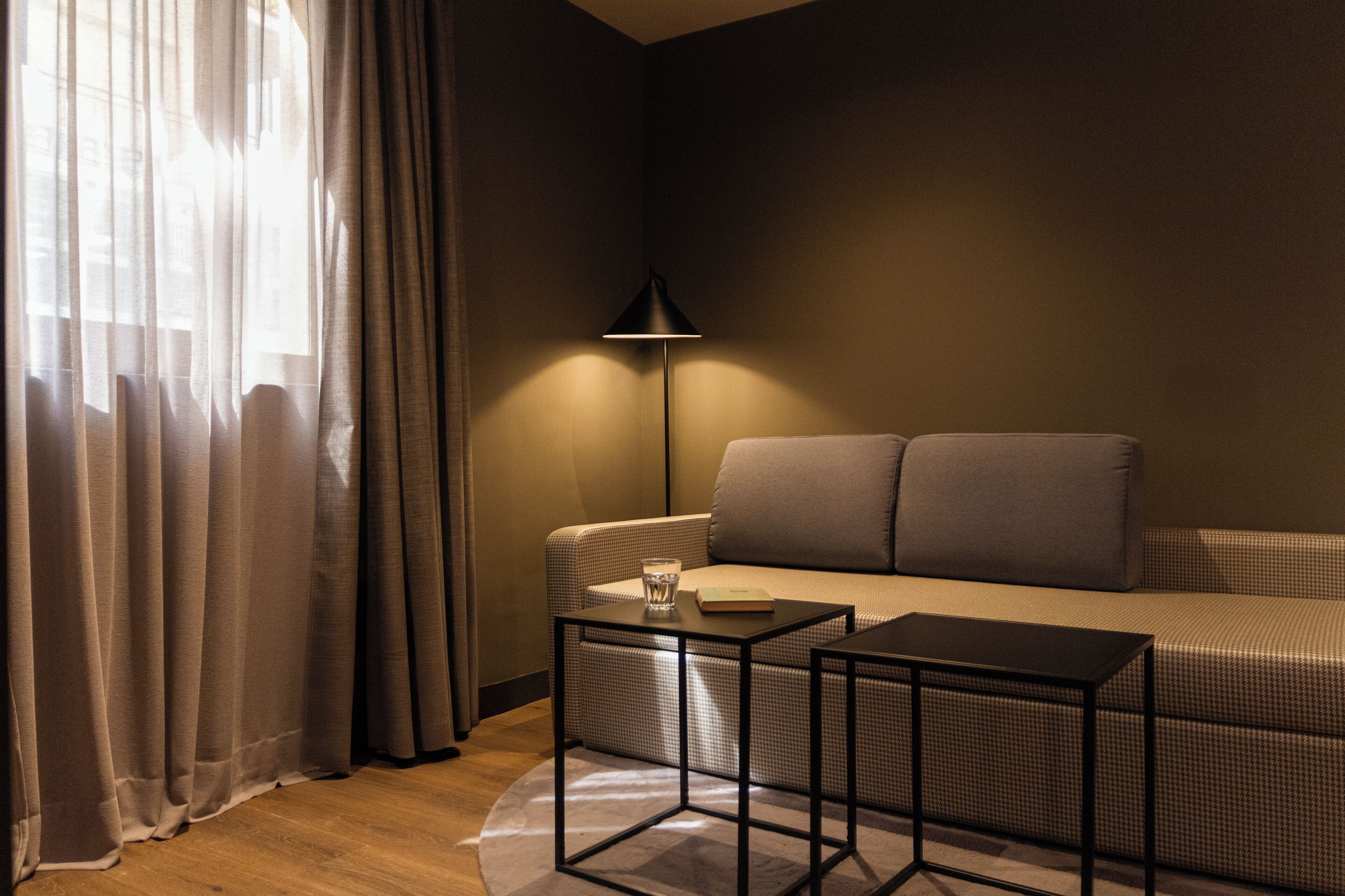 A modern hotel room with a sofa, a small table, and a floor lamp.