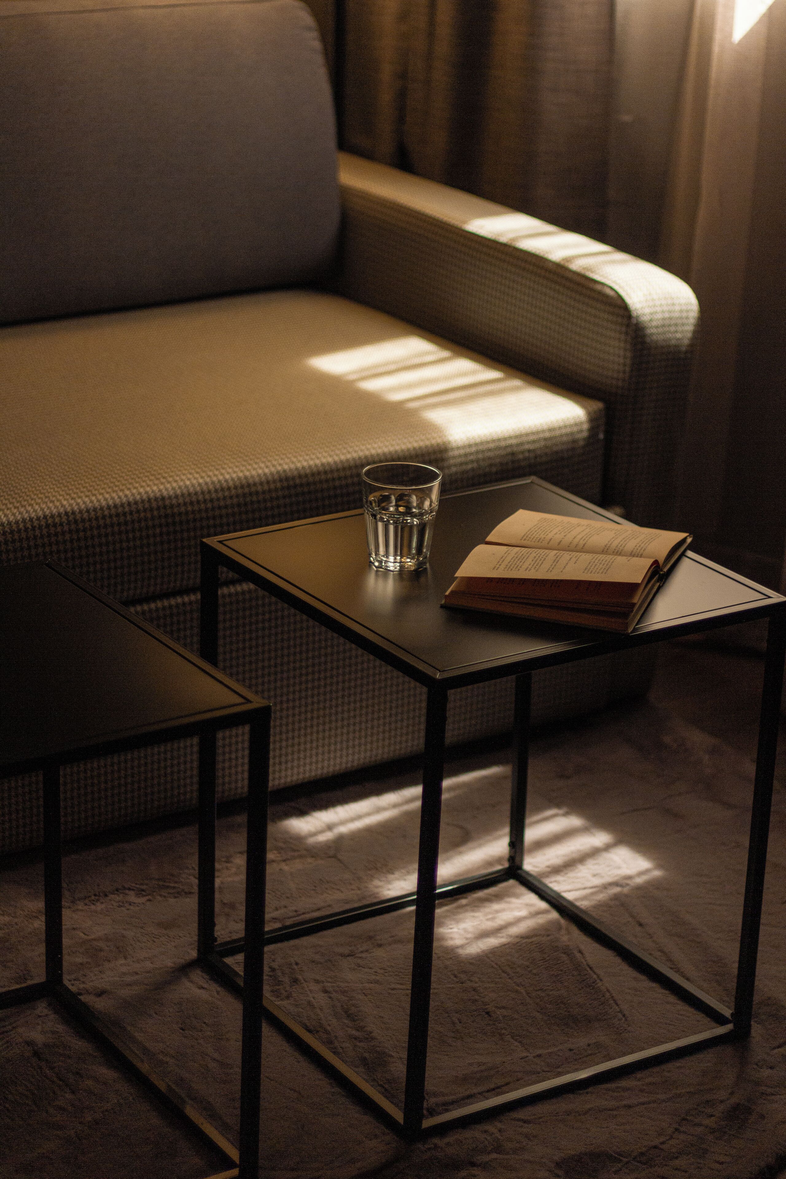 A small table with a glass of water and an open book, placed on a wooden floor near a sofa.