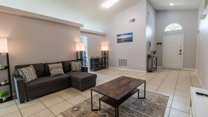 A modern living room with a sofa, ottoman, and coffee table. There are two lamps, a painting, and a door with a window. - 173 Hillside Dr in Davenport (Davenport)