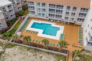 A hotel with a central swimming pool, multiple balconies, and a beach area with lounge chairs. - Pelican's Watch Unit 102 - Oceanfront (Myrtle Beach)