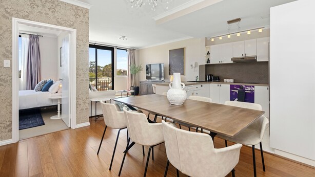 A modern kitchen with a dining area, a large white vase, and a chandelier. - Stunning 3BR Perth Penthouse (East Perth)