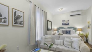 Una habitación de hotel moderna con una cama grande, un sofá y una mesa de centro. Hay cuadros enmarcados en la pared, una ventana con cortinas y un equipo de aire acondicionado.