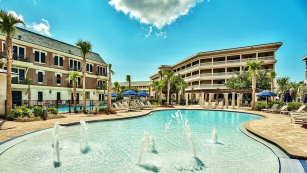 Un hotel con piscina, palmeras y un cielo azul despejado.