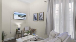 Una sala de estar moderna con un sofá blanco, un televisor de pantalla plana y una mesita auxiliar con una lámpara.
