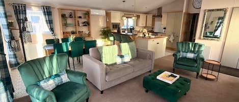 A living room with a sofa, two armchairs, and a coffee table. There is a kitchen in the background with a dining area.