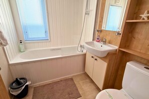 Un baño con bañera, lavamanos, inodoro y una ventana con persianas.