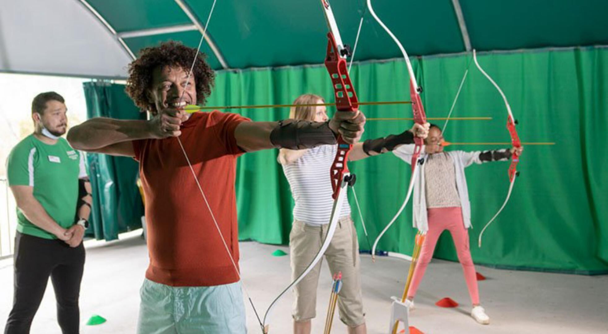 Un campo de tiro con arco en interiores, con participantes vestidos de verde.