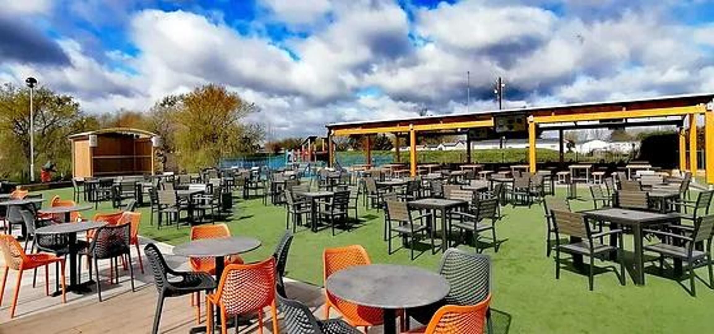 An outdoor patio area with multiple tables and chairs, a covered seating area, and a pool in the background.