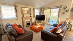 A living room with a fireplace, a television, and two sofas. - Sunset 19 - Southview Holiday Park Skegness (Skegness)