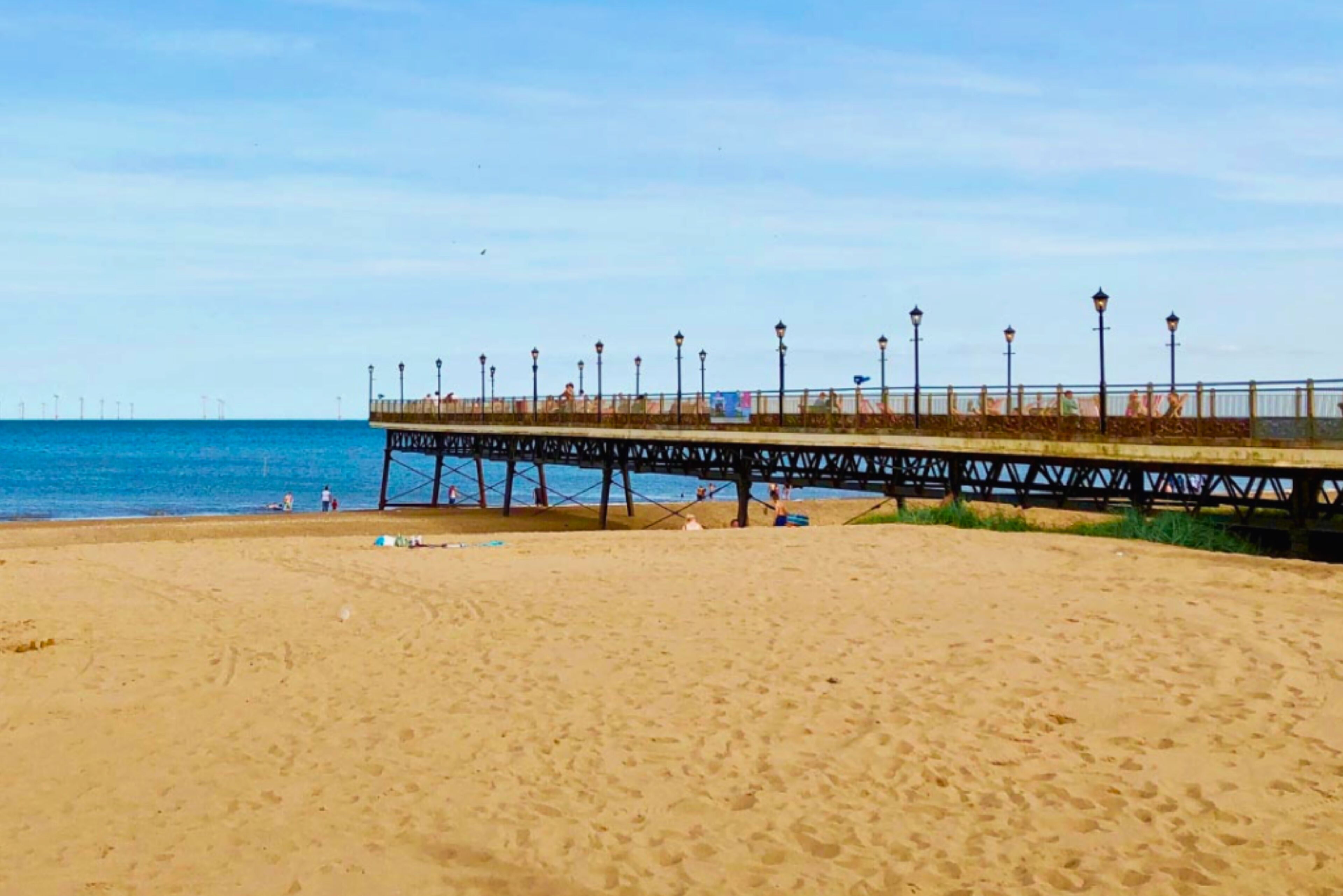 Une plage avec une jetée qui s’avance dans l’eau, agrémentée de lampadaires et d’une promenade.