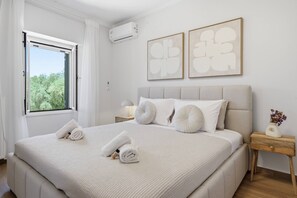 A modern bedroom with a large bed, a window with curtains, a bedside table with a lamp, and two wall-mounted abstract paintings. - Moute House by Corfuescapes (Corfu)