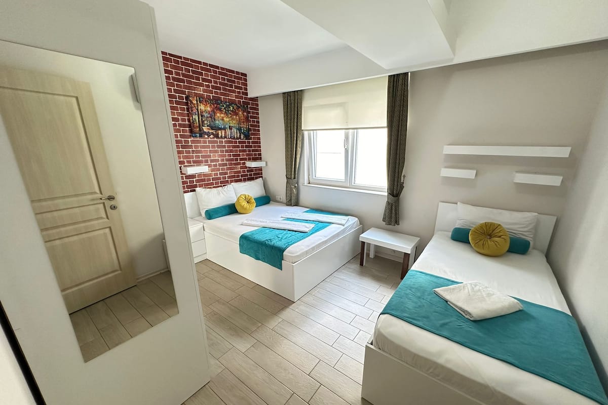 Een moderne hotelkamer met een accentmuur van baksteen, twee bedden, een klein tafeltje en een raam met gordijnen.