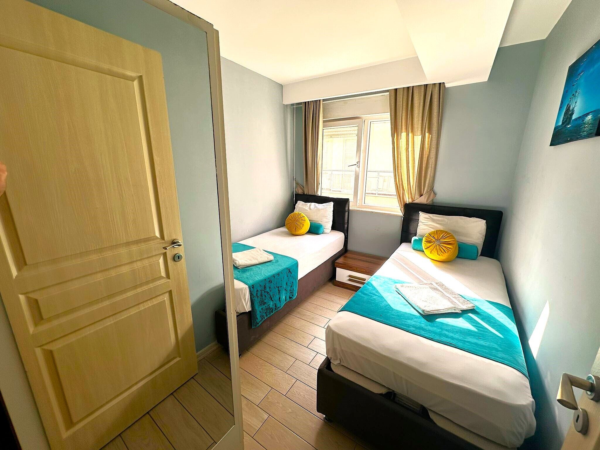A hotel room with two beds, a window with curtains, and a door.