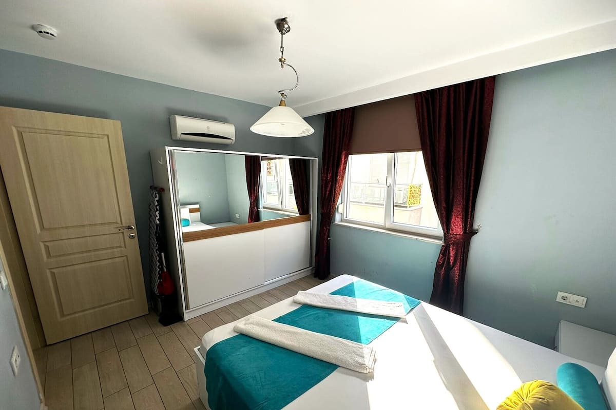 Een slaapkamer met een bed, een garderobe, een spiegel, een airconditioning en een raam met gordijnen.