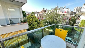 A balcony with a glass railing, a white table, and yellow chairs.