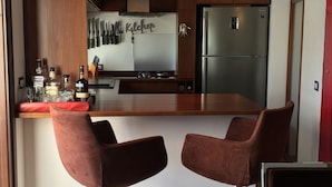 Una cocina moderna con una isla central, electrodomésticos de acero inoxidable y dos taburetes de bar.