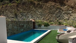 Una piscina con muro de piedra, césped artificial y mobiliario exterior.