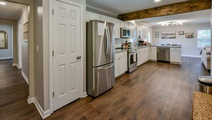 Una cocina amplia con armarios blancos, electrodomésticos de acero inoxidable y una viga de techo de madera.