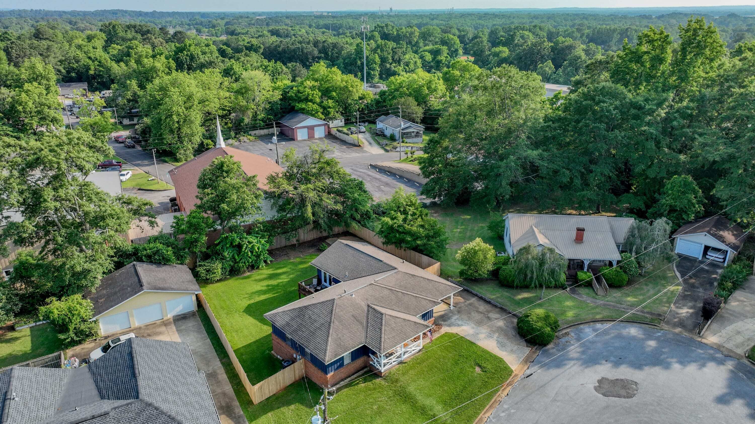An aerial view of a residential area with houses, lawns, and a clear sky.