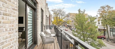 Ein Balkon mit Blick auf eine Straße, ein Backsteinhaus und ein Geschäft.