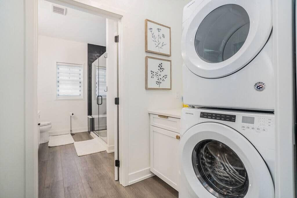 A laundry room with a stacked washer and dryer, a glass shower enclosure, and framed botanical prints on the wall.