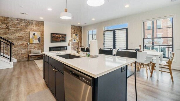 A modern kitchen with a central island, pendant lighting, and a dining area with a view.