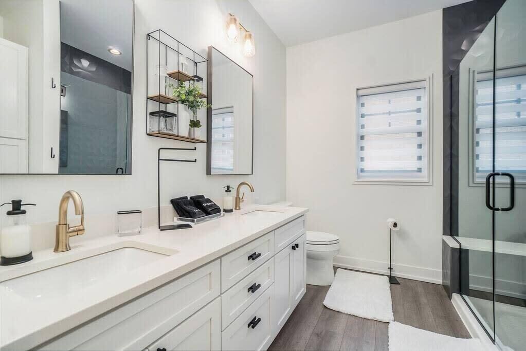 A modern bathroom with a large mirror, dual sinks, and a glass shower enclosure.