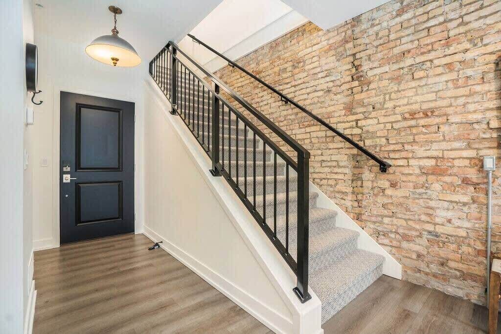 Un escalier avec une rampe en métal noir mène à une pièce dont le mur est en pierre et le plancher en bois.