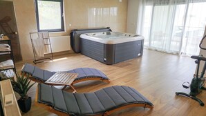 A modern room with a hot tub, two lounge chairs, a small table, and a treadmill.