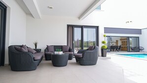 A modern outdoor living area with wicker furniture, a pool, and a view of the adjacent building.
