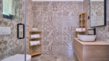 A bathroom with patterned tiles, a wooden shelf with towels, a white sink with a black faucet, and a mirror on the wall.
