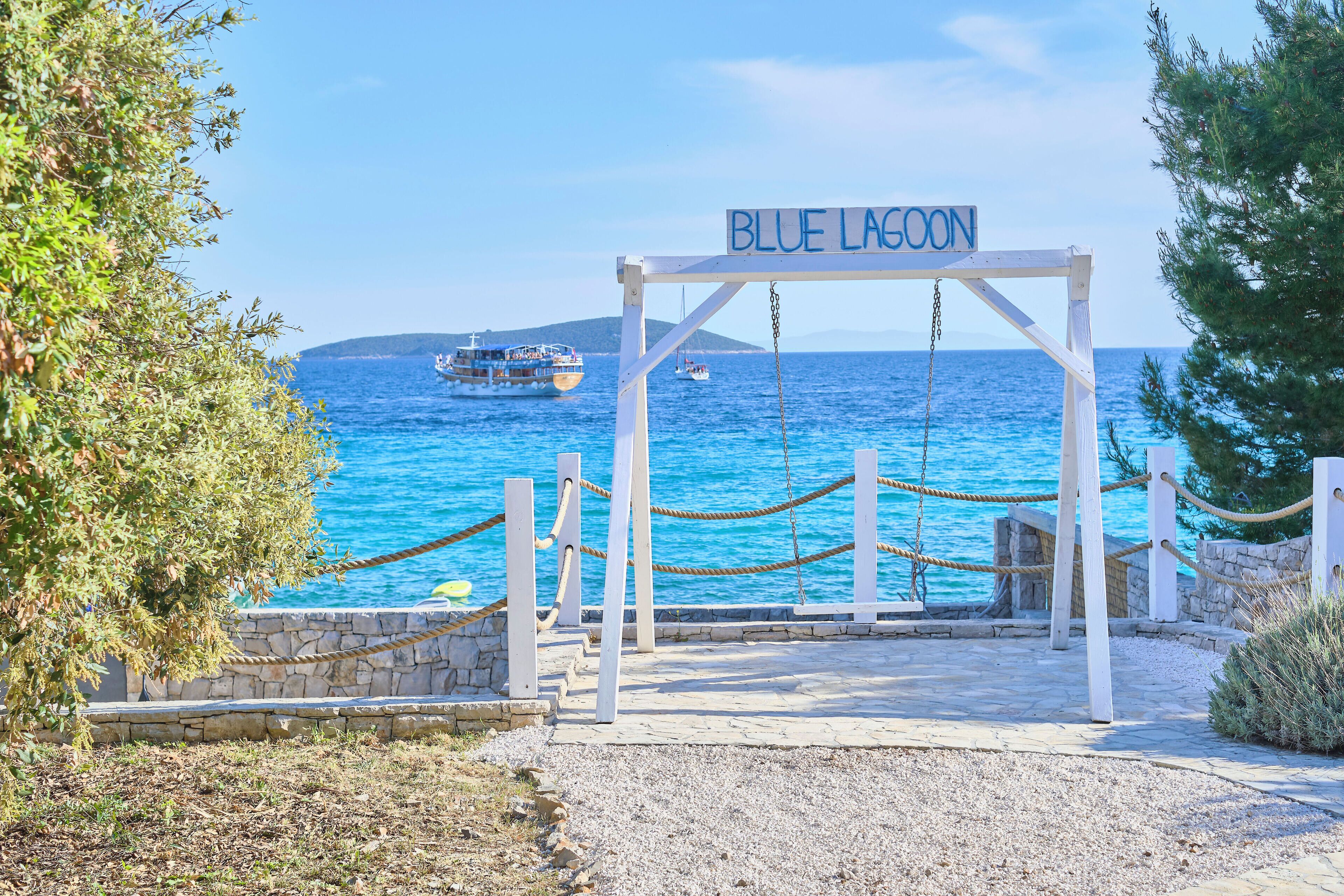 Ein Schild mit der Aufschrift 'BLUE LAGOON', im Hintergrund Meer und Boote.