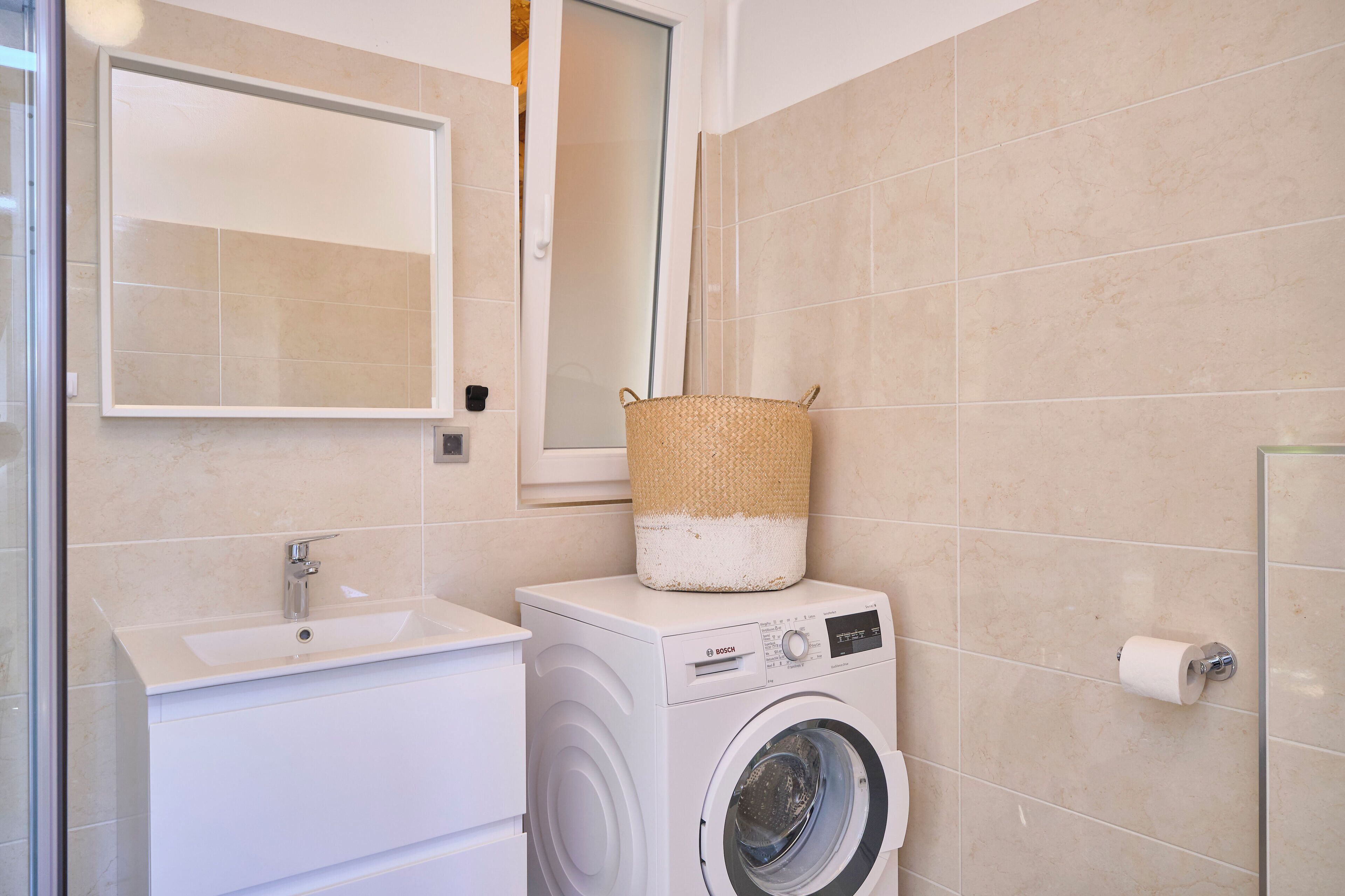 Ein kleines Badezimmer mit Waschmaschine, Waschbecken und Spiegel.