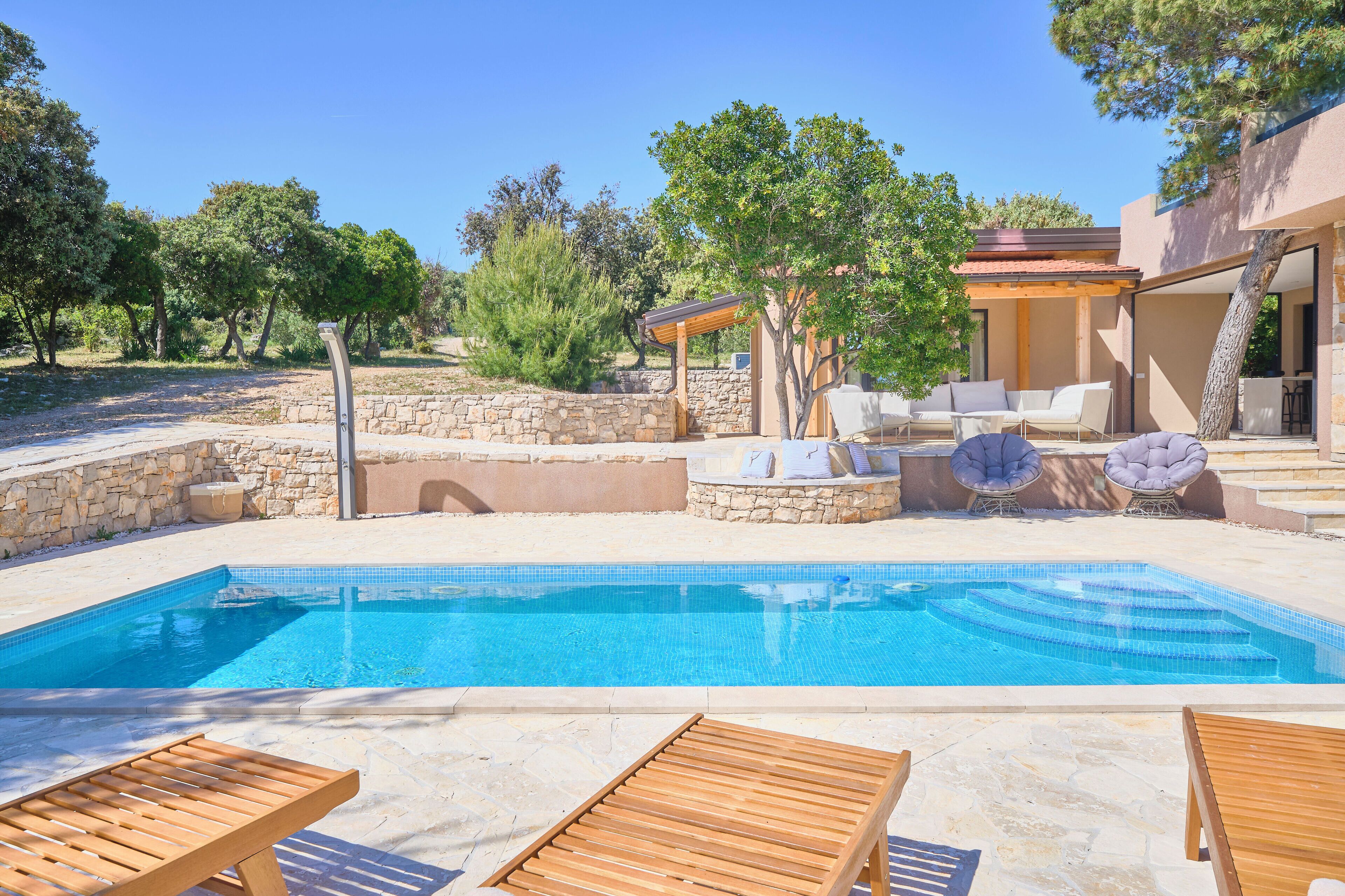 A swimming pool with wooden loungers, stone walls, and outdoor furniture.