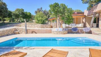 A swimming pool with wooden loungers, stone walls, and outdoor furniture.