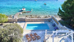 A pool area with lounge chairs, a stone wall, and a view of the sea with boats. - Resort Amalka Mare by Litto (Trogir)