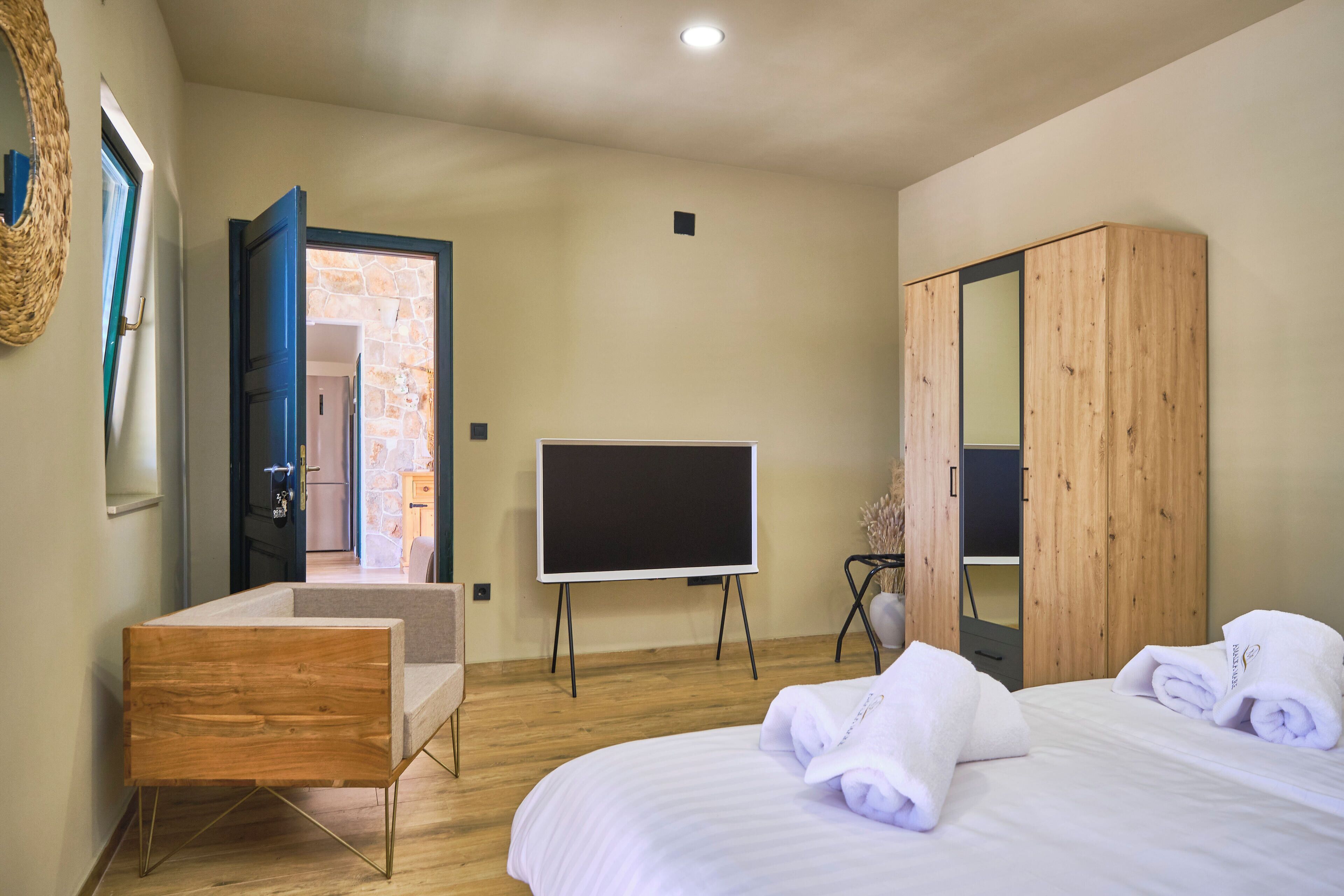 A bedroom with a bed, a wooden wardrobe, a television on a stand, and a door leading to a stone-walled room.