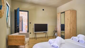 A bedroom with a bed, a wooden wardrobe, a television on a stand, and a door leading to a stone-walled room.