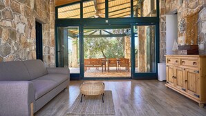 A spacious room with a stone wall, a wooden ceiling, a sofa, a wicker chair, a wooden cabinet, and a glass door leading to an outdoor patio with a table and chairs. - Resort Amalka Mare by Litto (Trogir)