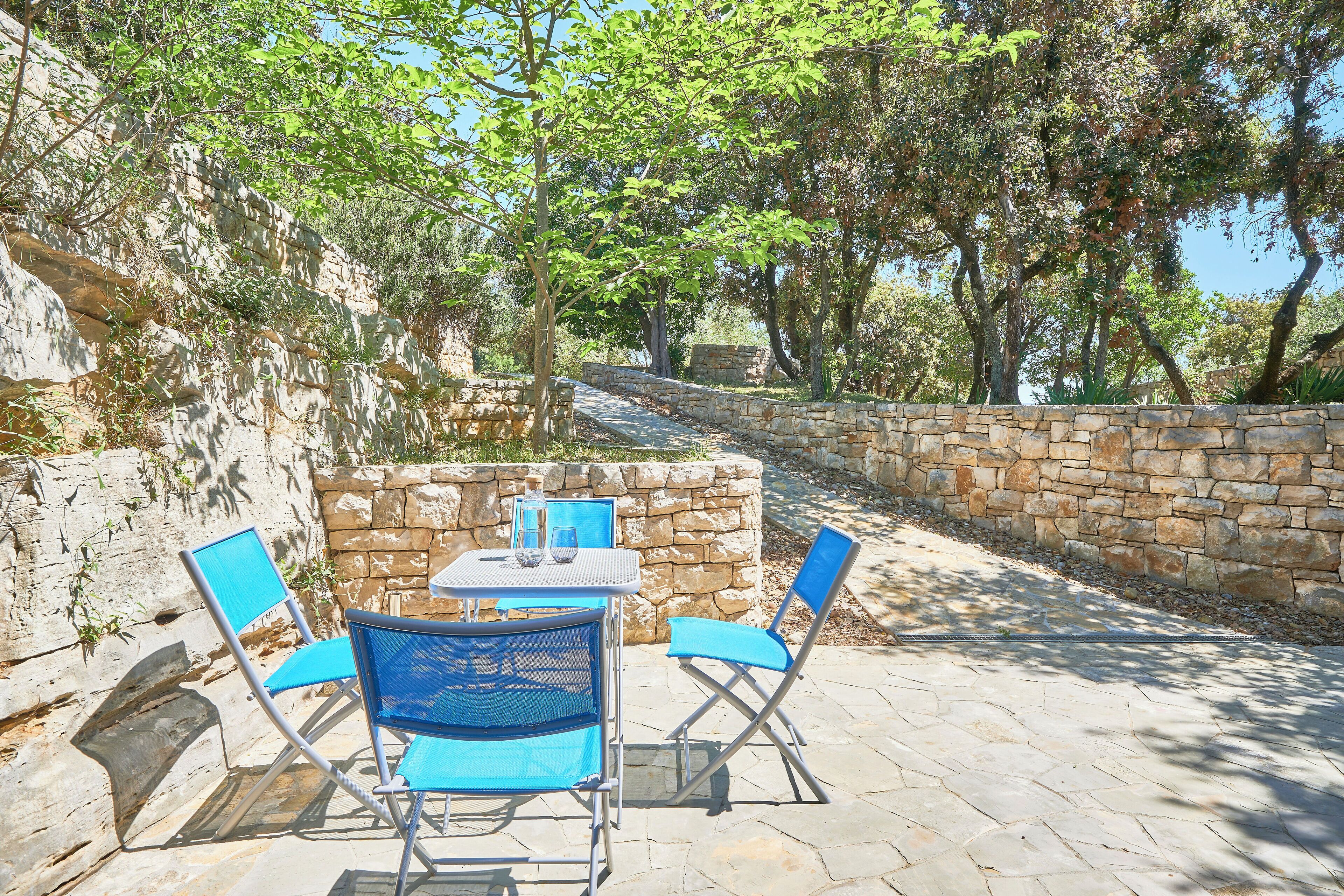 An outdoor patio with stone walls, a table, and blue chairs.