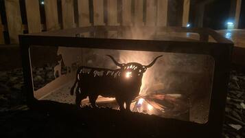 A metal fire pit with a silhouette of a bull and a small fire inside.