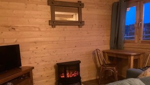 Interior acollidor d'una cabana amb paret de fusta, una llar de foc, televisió, sofà i taula de menjador.