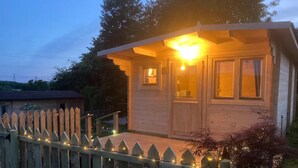 Una cabana de fusta amb un porxo, una tanca de palets i llums penjants.