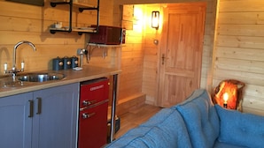 A compact kitchen with a sink, a red refrigerator, and a microwave. There is a wooden door and a clock on the wall. - Cosy 1-bed Farm Stay Cabin (Chesterfield)