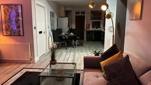 A modern living room with a glass coffee table, a sofa with cushions, a dining area with chairs, and a kitchen in the background. - 1 Bed Flat - Sleeps 2 - Jacuzzi - Parking - Wifi (Birmingham)