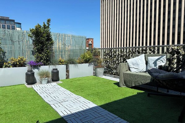 A rooftop garden with artificial grass, a pathway, potted plants, and a seating area with cushions. - 1 Bed Penthouse - Hot Tub - Roof Terrace - Parking (Birmingham)