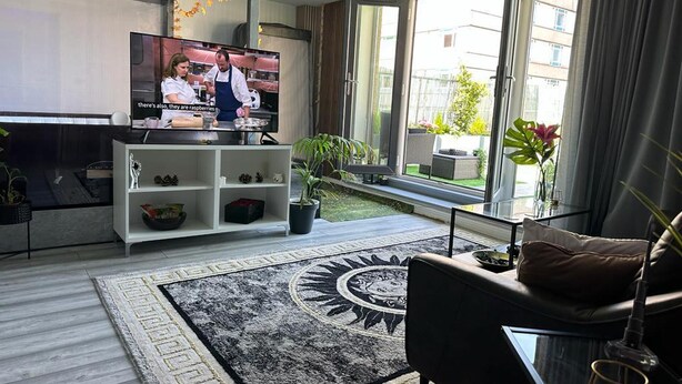 Una sala de estar moderna con un televisor grande, un sofá, una mesa de centro y vistas al exterior a través de amplios ventanales.