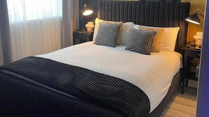 Una cama bien hecha con colcha y almohadas negras, una lámpara de noche y una mesita de noche con lámpara.